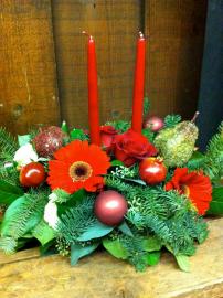 Christmas Centerpiece with ornamental fruit, Gerber daisies, red roses, and a variety of x-mas greens.